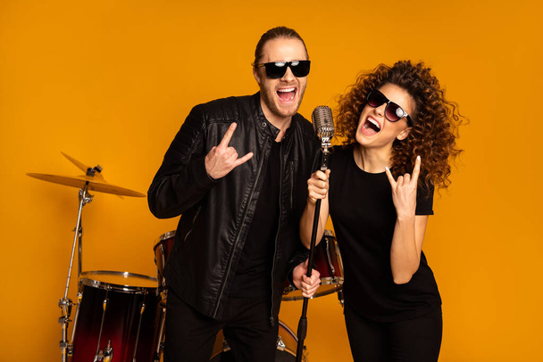 Photo of two people cool handsome guy attractive lady girl sing retro old fashion mic concert show horns fingers drum instruments wear trendy rocker leather outfit isolated yellow background - Фото, изображение
