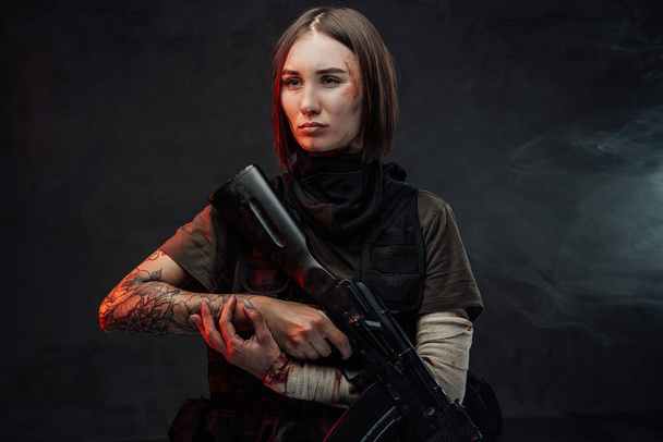Kolu bandajlı kadın asker, elinde siyah arka planda bir tüfek var. - Fotoğraf, Görsel