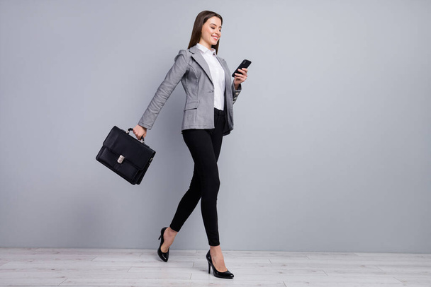 Full size profile photo of slim pretty business lady young chief hold diplomat bag browsing telephone go meeting wear plaid blazer trousers high-heels isolated grey color background - Photo, Image