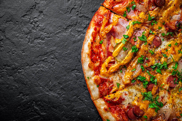 Pizza with Mozzarella cheese, backon, ham, tomato sauce, pepper, sausage, pickled cucumbers and onion. Italian pizza on Dark grey black slate background - Foto, Bild