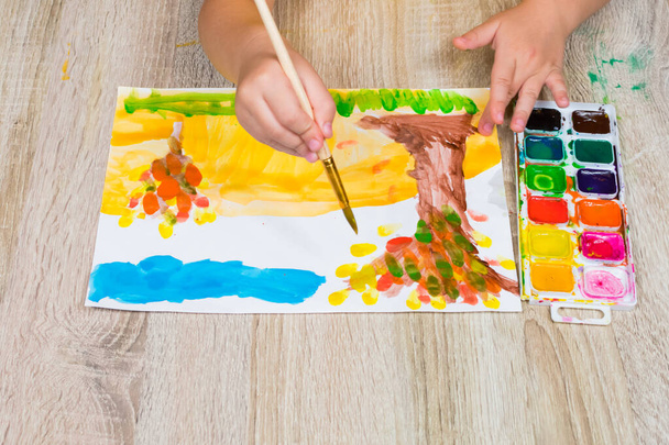 Lapsi piirtää syksyn penzage akvarelleilla. Lähikuva lapsen käsi harjalla ja akvarelleja. Lasten taiteilija kiinnittää, luovuus, virkistys, koulutus, piirustus, värikurssit - Valokuva, kuva