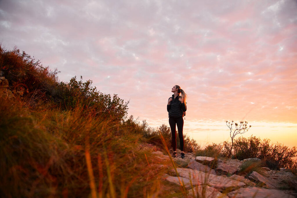 Vista frontale della giovane donna in vacanza che indossa lo zaino che parte per il sentiero escursionistico in campagna al tramonto - Foto, immagini