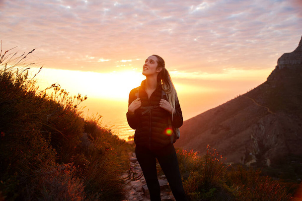 Vista frontale della giovane donna in vacanza che indossa lo zaino in partenza per il sentiero costiero di arrampicata al tramonto - Foto, immagini
