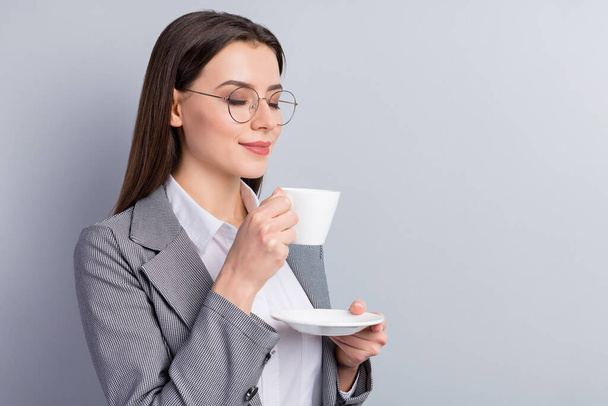 Closeup photo of attractive business lady manager hold white porcelain cup plate drink hot coffee enjoy nice smell eyes closed wear specs shirt plaid blazer isolated grey color background - Фото, зображення