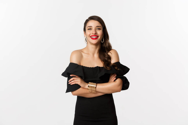 Beauty and fashion concept. Attractive female model in party dress and red lipstick, smiling pleased, looking happy, standing over white background - Photo, Image