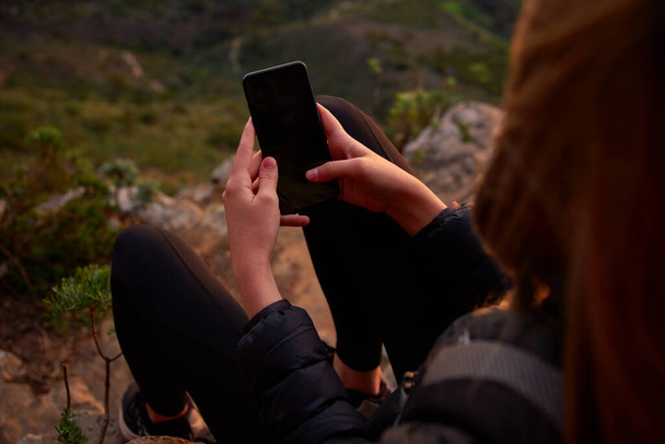 Primo piano della donna in vacanza che cammina lungo il sentiero di campagna al tramonto o all'alba controllando i messaggi sui social media con il telefono cellulare - Foto, immagini
