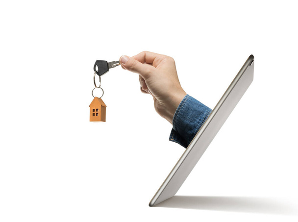 人間の手に紙の家の鍵は、デジタルタブレット画面の外に固執する。不動産業界における近代技術の概念.  - 写真・画像