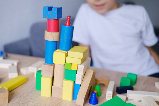 kid, boy builds towers and buildings from colored wooden figures, concept of housing construction, mortgage, insurance, happy childhood, children's games - Foto, Bild
