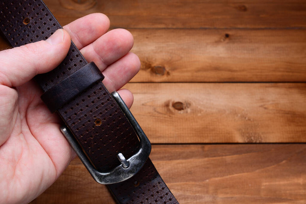 brown belt in a man's hand on a wooden background. copy space. - 写真・画像