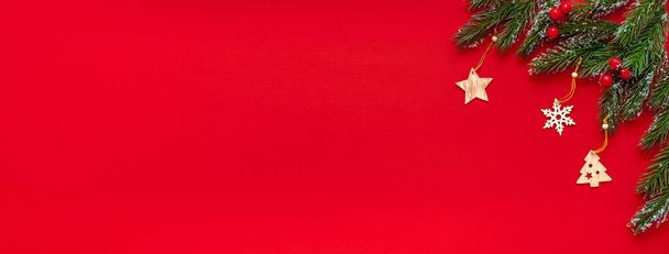 Fir takken, houten kerstspeelgoed op een rode achtergrond.Kerst of nieuwjaar achtergrond met tekst plaatsing - Foto, afbeelding