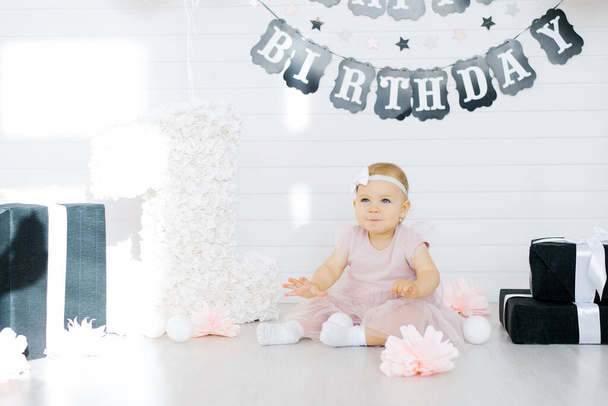 Urodziny dziewczyna 1 rok siedzi w strefie fotograficznej otoczony przez prezenty, kwiaty - Zdjęcie, obraz