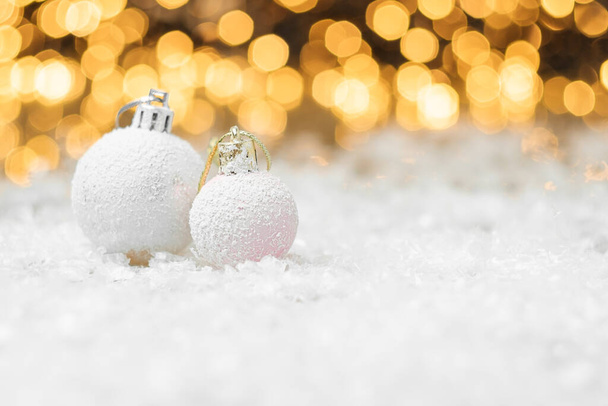 背景に黄色のライトボケで雪の中に横たわる装飾的なクリスマスボール。コピースペース付きのお正月やパーティーのためのグリーティングカード. - 写真・画像