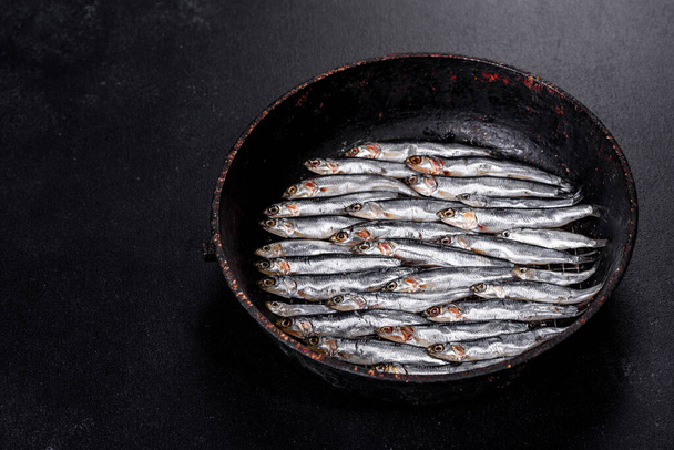 Several fish salted anchovies on a dark concrete table. Concept of small fish - Фото, изображение