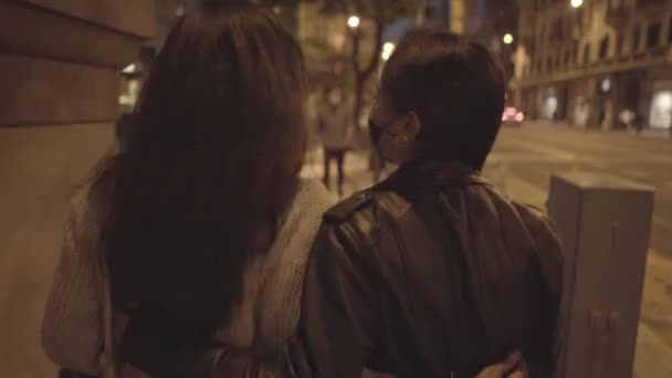 View from behind of two young black women friends walking at night in the city with facial mask. - Materiał filmowy, wideo