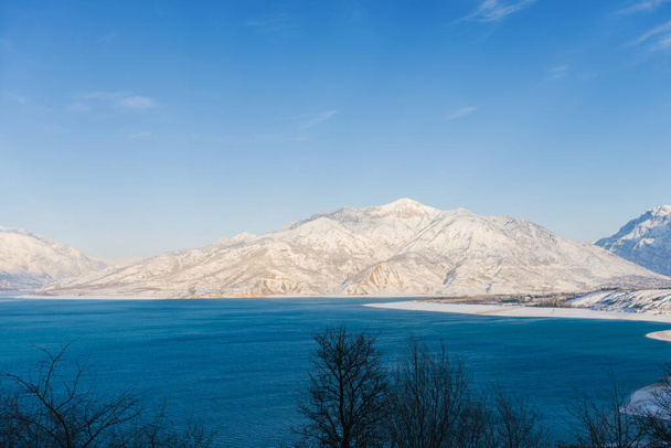 ウズベキスタンの晴れた冬の日に青い水のシャルヴァク貯水池 - 写真・画像