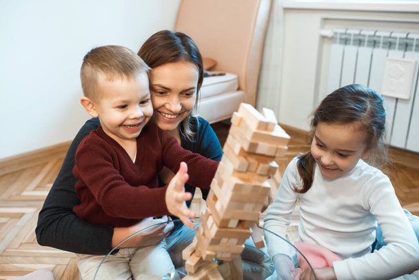 Caucasian mother and her son and little girl playing jenga on the glass table smiling together - 写真・画像