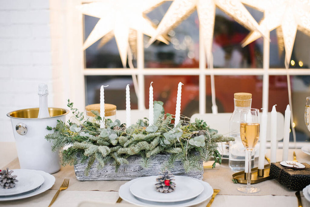 Lindo conjunto de mesa com decorações, velas e lanternas. A sala de estar está decorada com guirlandas e uma árvore de Natal. Ambiente festivo - Foto, Imagem