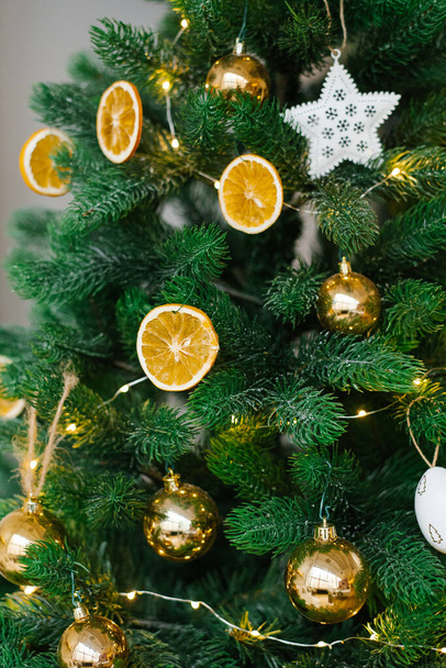 Der Weihnachtsbaum ist geschmückt mit Spielzeug, getrockneten Zitronen oder Orangen, goldenen Kugeln, weißen Eiern und Girlanden in Großaufnahme. - Foto, Bild
