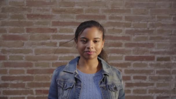 Porträt einer schwarzen Afroamerikanerin, die vor einer Backsteinwand in die Kamera lächelt. - Filmmaterial, Video