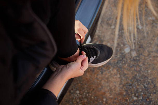 close-up van jonge vrouw op reis zitten in open achterklep van auto koppelverkoop schoenen alvorens af te gaan op wandeling in het platteland tegen blauwe lucht - Foto, afbeelding