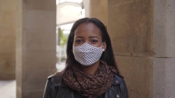 Retrato de una mujer negra afroamericana con máscara facial mirando a la cámara al aire libre. Nueva normalidad en tiempos de coronavirus debido a la pandemia de covida19. - Imágenes, Vídeo