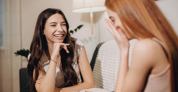 Laughing caucasian women are talking on the couch while smile and having joy - Φωτογραφία, εικόνα