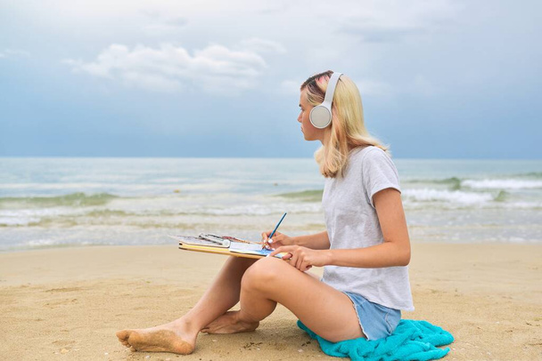 Teenager girl in headphones drawing with watercolors marine sketch - Fotó, kép