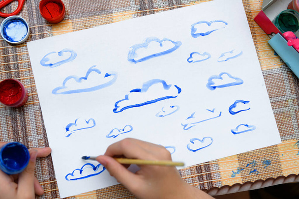 uma menina desenhando nuvens azuis aquarela em um papel branco em branco, criação artística em casa, faz arte criativa - Foto, Imagem
