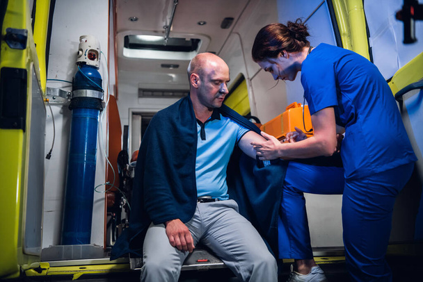 Una giovane infermiera in uniforme che fa un'iniezione ad un paziente in un'ambulanza - Foto, immagini