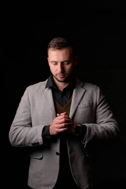 Studioporträt eines jungen kaukasischen Mannes im schwarzen Blazer, der in die Kamera blickt und vor schlichtem Studiohintergrund steht - Foto, Bild