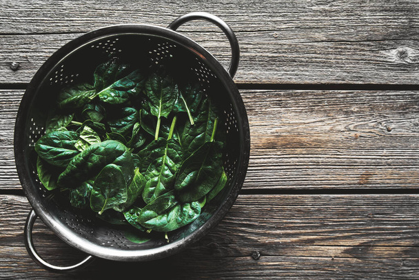 Fresh spinach in metal colander on wooden background. Healthy food, vegan - Foto, Bild