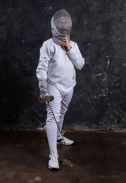 Teenage girl fencer dressed in uniform with epee and helmet - Foto, afbeelding