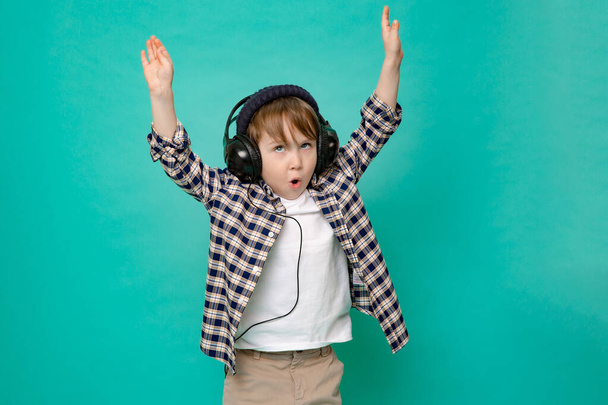cute 4-5 year old boy in shirt and baseball cap listening to music with headphones on isolated green background - Zdjęcie, obraz