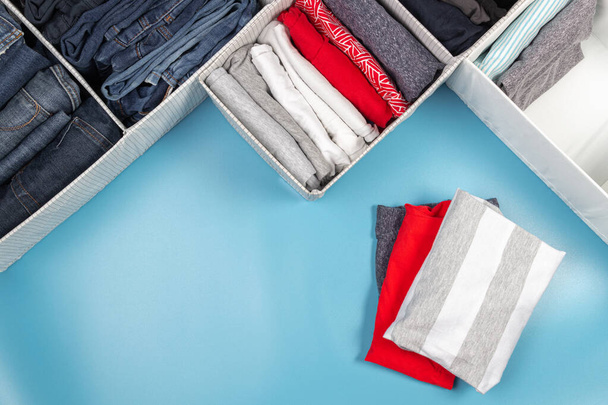 Vertical storage of clothing, tidying up, room cleaning concept. Stack of folded clothes in basket over light blue background. Top view - Photo, Image