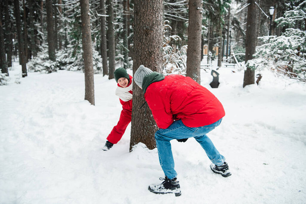 ein Mann in roter Jacke im Winterwald beim Nachholen mit seinem Neffen, ein Junge in rotem Winteranzug und Schal - Foto, Bild