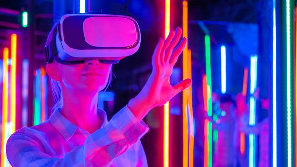 Jeune femme utilisant un casque de réalité virtuelle à l'exposition VR interactive sombre - Photo, image
