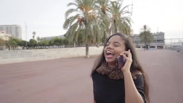 Boldog és mosolygós fiatal fekete nő az utca közepén beszél telefonon és nevet. Orbitális lövés.. - Felvétel, videó