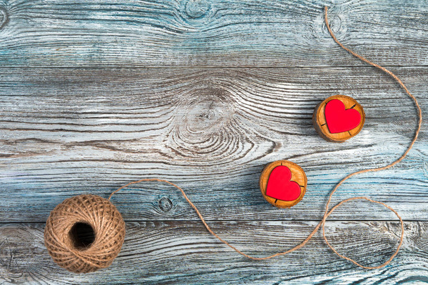 Zwei rote Herzen auf Holzständern mit Jutefaden auf grau-blauem Hintergrund. - Foto, Bild