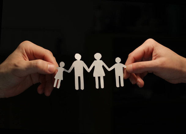 Eine Papierfamilie hält sich an den Händen und formt eine Kette, wobei eine männliche und eine weibliche Hand an den Seiten sie an der Hand halten, mit dem Zeichen der Vereinigung. - Foto, Bild