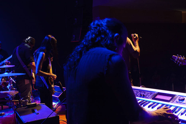 Музыканты создают музыку, играя на клавишных гитарах, бас-гитаре, барабанах, вокализируя в Мехико с синим освещением - Фото, изображение
