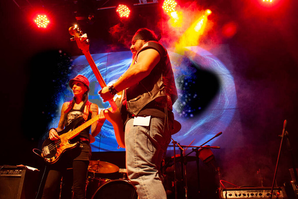 Pair of people woman bassist playing bass strings and man guitarist playing guitar among artificial fog in Mexico city setting nightlife - Photo, Image