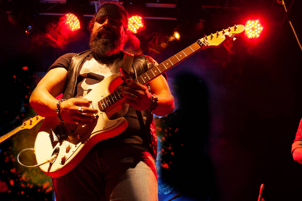 bearded man with bandana tied to his head playing guitar strings exploring musical nightlife in Mexico city illuminated with red light - Photo, Image