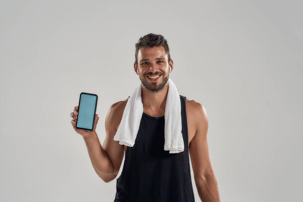 Happy young muscular caucasian man showing smartphone - Zdjęcie, obraz