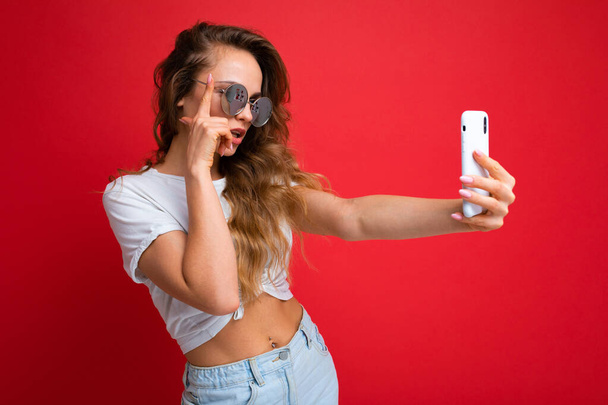 Primer plano retrato agradable-buscando encantadora dama atractiva toma selfie aislado sobre brillante brillante brillo fondo rojo - Foto, imagen