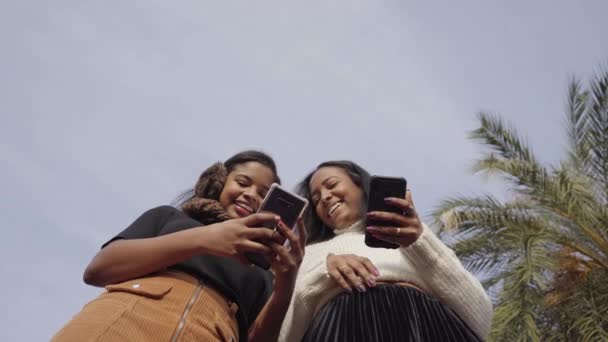 Lage hoek van twee zwarte meisjes met behulp van een mobiele telefoon en lachen. Mensen en technologie concept met smartphone. - Video