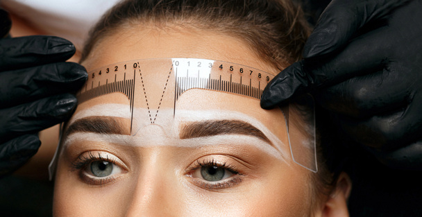 Cosmetician making measuring with ruler and getting ready to apply makeup to a client. Closeup shot - Photo, Image