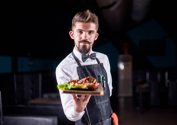 Χαρισματικός σερβιτόρος σερβίρει πιάτο σε εορταστική εκδήλωση. - Φωτογραφία, εικόνα