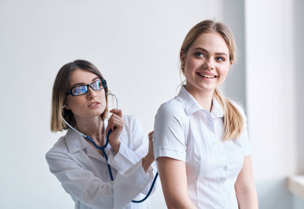 Donna donna donna delle pulizie in abito medico ascolta il battito cardiaco dei pazienti su uno sfondo leggero - Foto, immagini