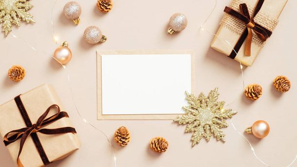 Christmas card mockup on pastel beige background with gift boxes, golden balls and xmas decorations. Flat lay, top view. Minimal style. - Photo, image