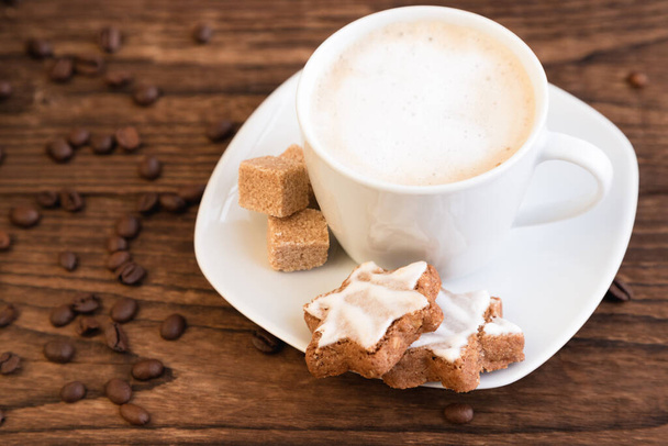 A cup, a mug of aromatic coffee with froth, sugar cubes and cookies on a saucer. Wooden background. Coffee shop advertisement, coffee break. Close-up. - Foto, Imagem